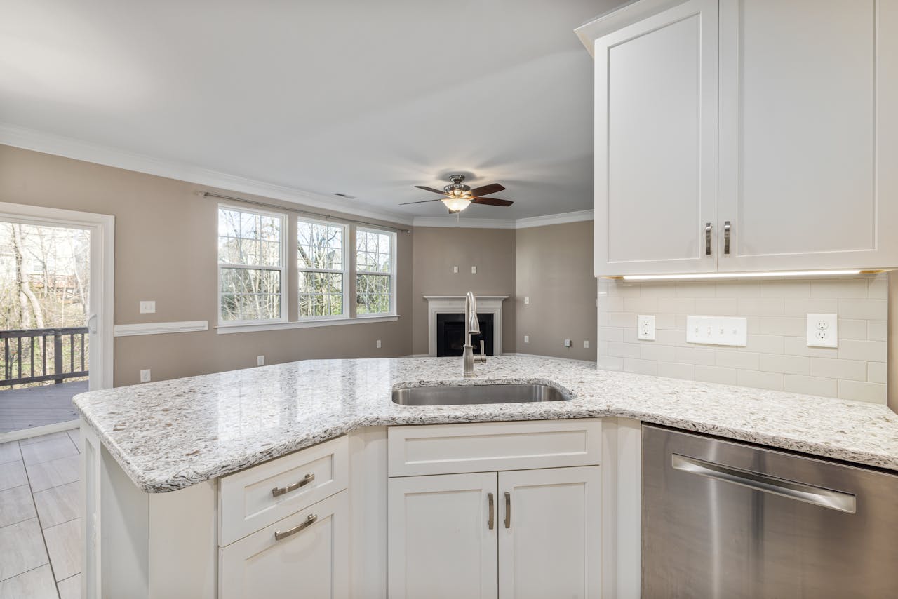 Spacious kitchen interior with white cabinets and granite countertops, featuring stainless steel appliances.